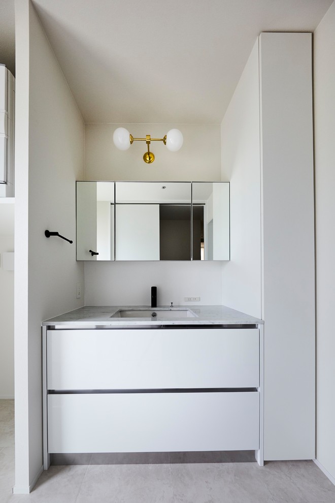 Moderne Gästetoilette mit flächenbündigen Schrankfronten, weißen Schränken, weißer Wandfarbe, integriertem Waschbecken und grauem Boden in Sonstige