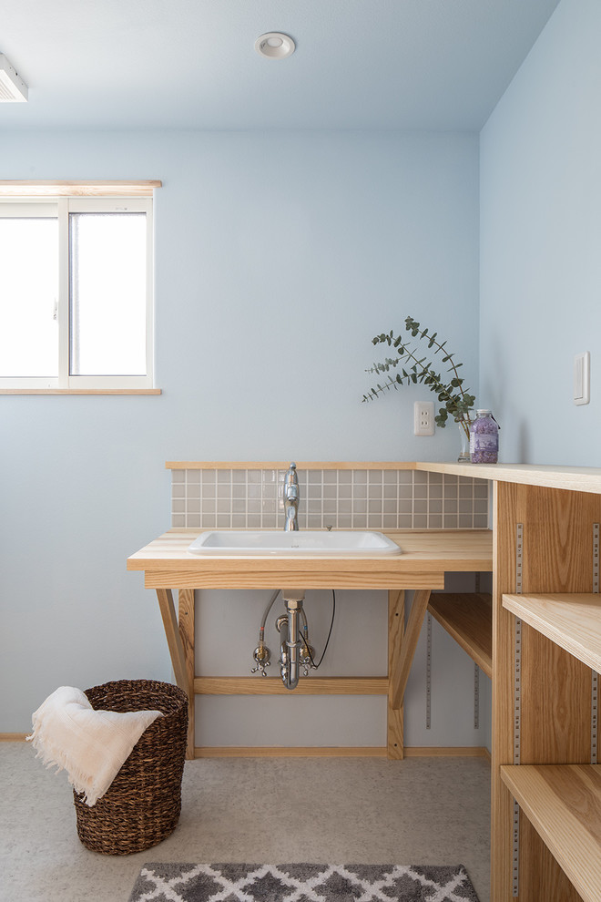 他の地域にある北欧スタイルのおしゃれなトイレ・洗面所 (オープンシェルフ、淡色木目調キャビネット、青い壁、オーバーカウンターシンク、木製洗面台、グレーの床、ベージュのカウンター) の写真
