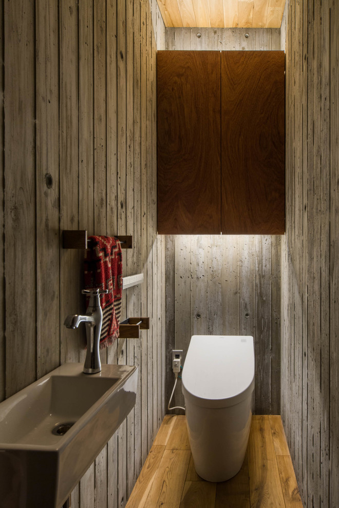 Industriell inredning av ett toalett, med grå väggar, mellanmörkt trägolv, brunt golv, släta luckor och skåp i mellenmörkt trä