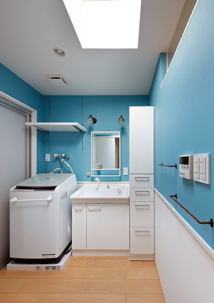 Foto de aseo escandinavo con armarios con paneles con relieve, puertas de armario blancas, paredes azules, suelo de madera clara, lavabo integrado, suelo beige y encimeras blancas