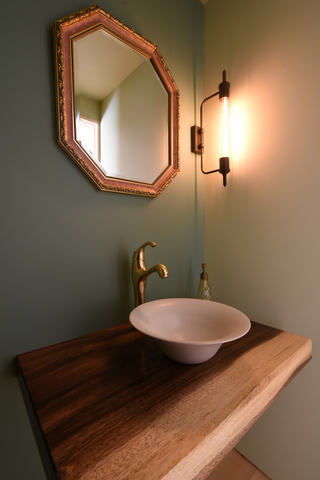Inredning av ett industriellt litet flerfärgad flerfärgat toalett, med en toalettstol med separat cisternkåpa, gröna väggar, mellanmörkt trägolv, ett nedsänkt handfat, träbänkskiva och flerfärgat golv