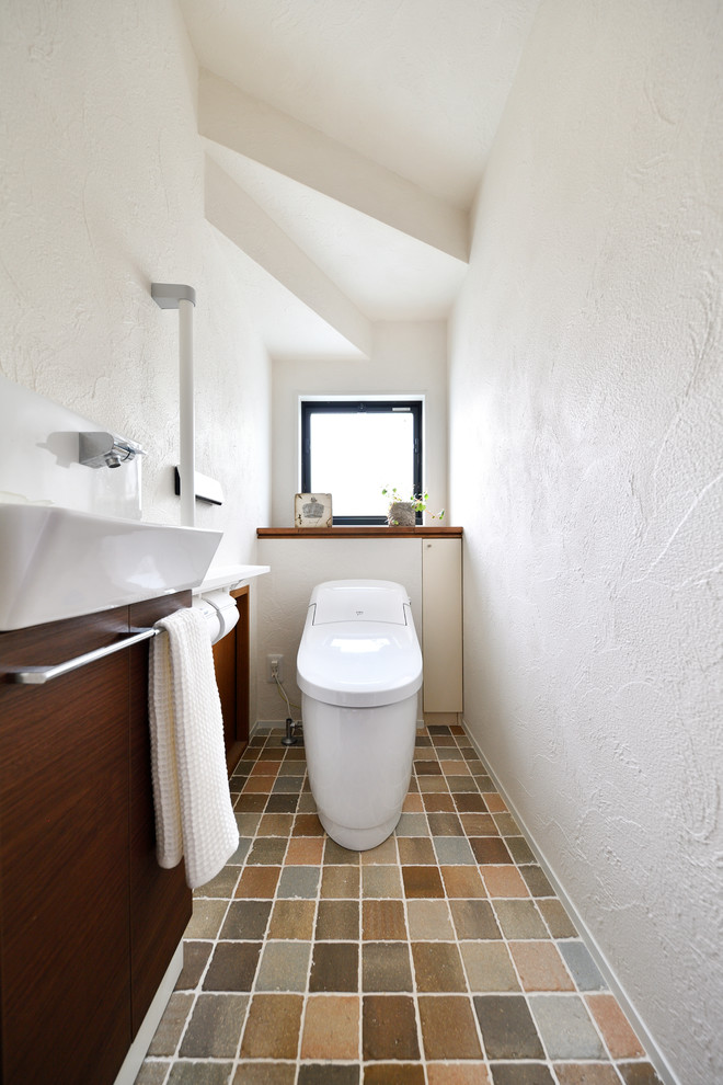 На фото: туалет в скандинавском стиле с плоскими фасадами, коричневыми фасадами, белыми стенами, настольной раковиной и коричневым полом