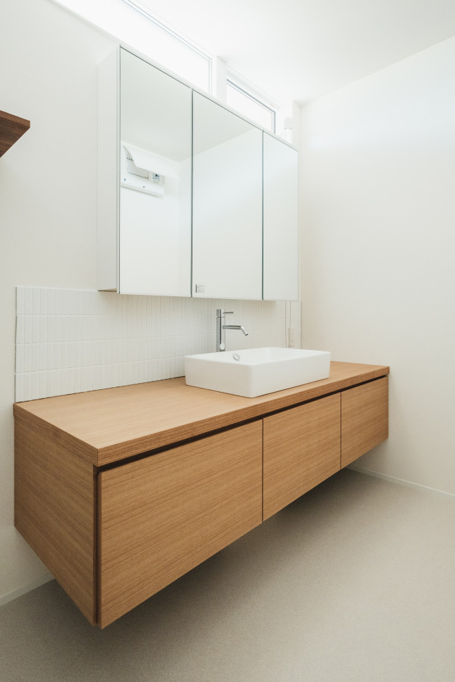 Idéer för mellanstora funkis brunt toaletter, med möbel-liknande, skåp i ljust trä, en toalettstol med hel cisternkåpa, vit kakel, porslinskakel, vita väggar, vinylgolv, ett fristående handfat och grått golv