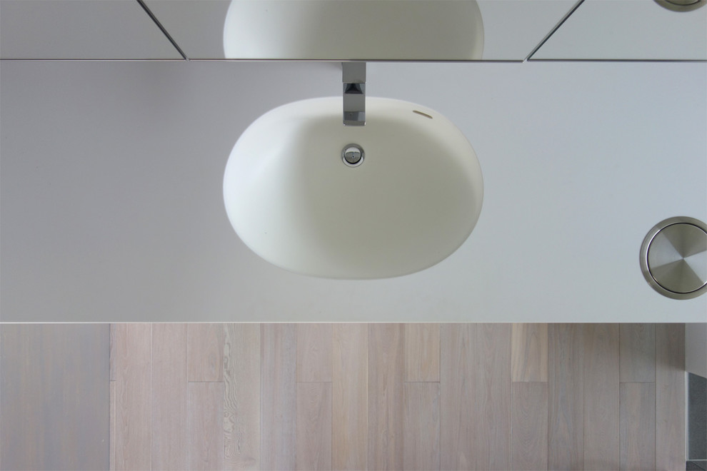 Moderne Gästetoilette mit Kassettenfronten, weißen Schränken, weißer Wandfarbe, hellem Holzboden, integriertem Waschbecken, Mineralwerkstoff-Waschtisch, weißem Boden und weißer Waschtischplatte in Tokio