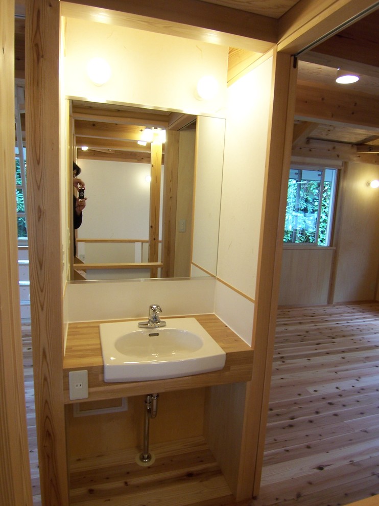Aménagement d'un petit WC et toilettes asiatique en bois brun avec un placard sans porte, un mur blanc, un sol en bois brun, un lavabo posé et un plan de toilette en bois.