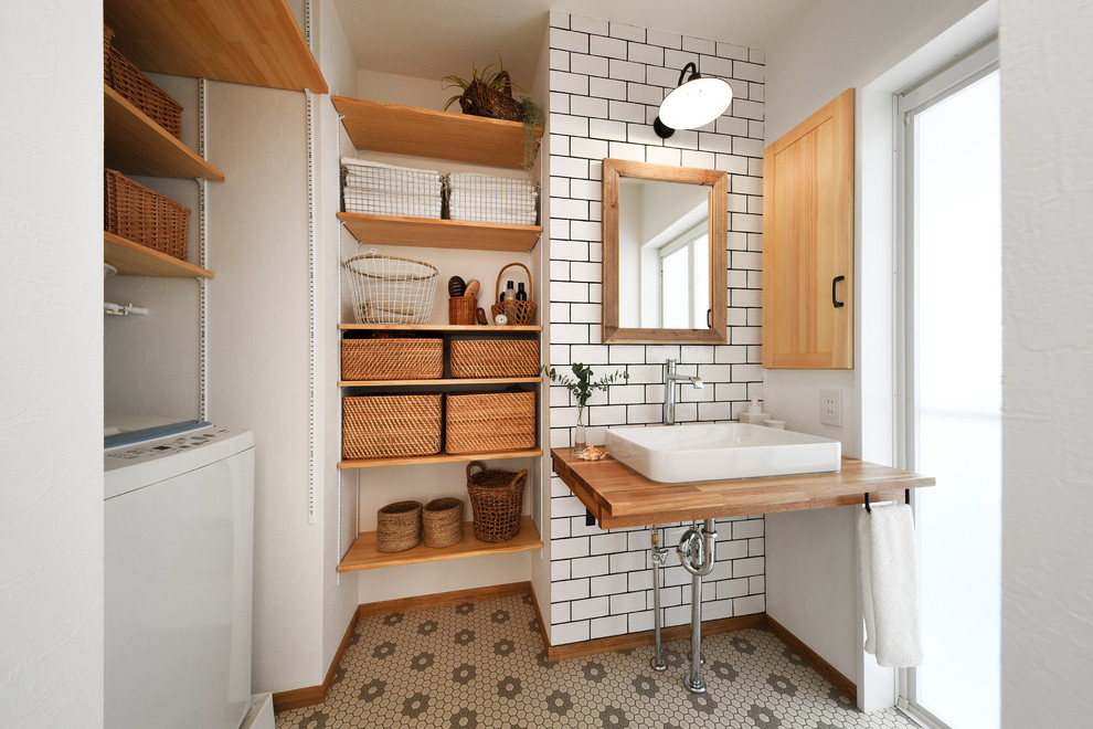 На фото: туалет в скандинавском стиле с открытыми фасадами, белыми стенами, настольной раковиной, столешницей из дерева, разноцветным полом и коричневой столешницей