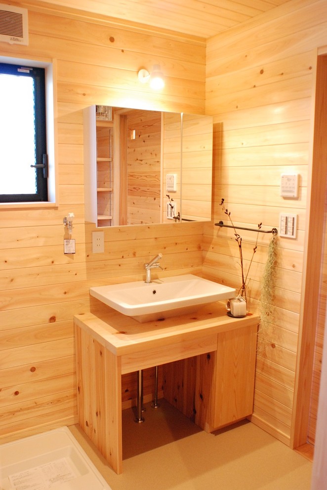 Photo of a small world-inspired cloakroom in Other with flat-panel cabinets, light wood cabinets, beige walls, a vessel sink, wooden worktops and beige floors.