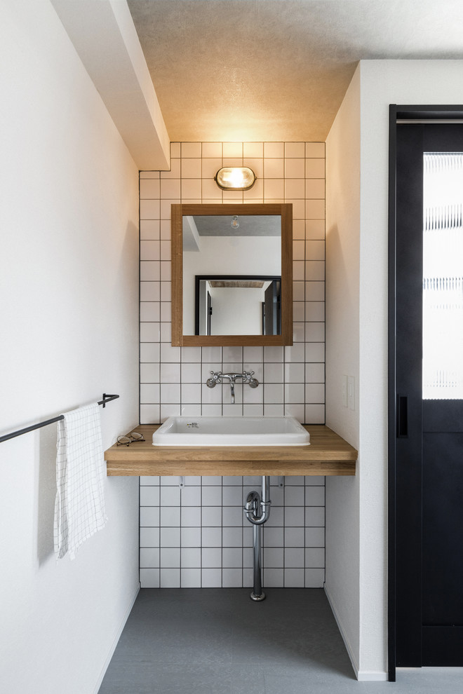名古屋にあるインダストリアルスタイルのおしゃれなトイレ・洗面所 (白いタイル、磁器タイル、白い壁、オーバーカウンターシンク、木製洗面台) の写真