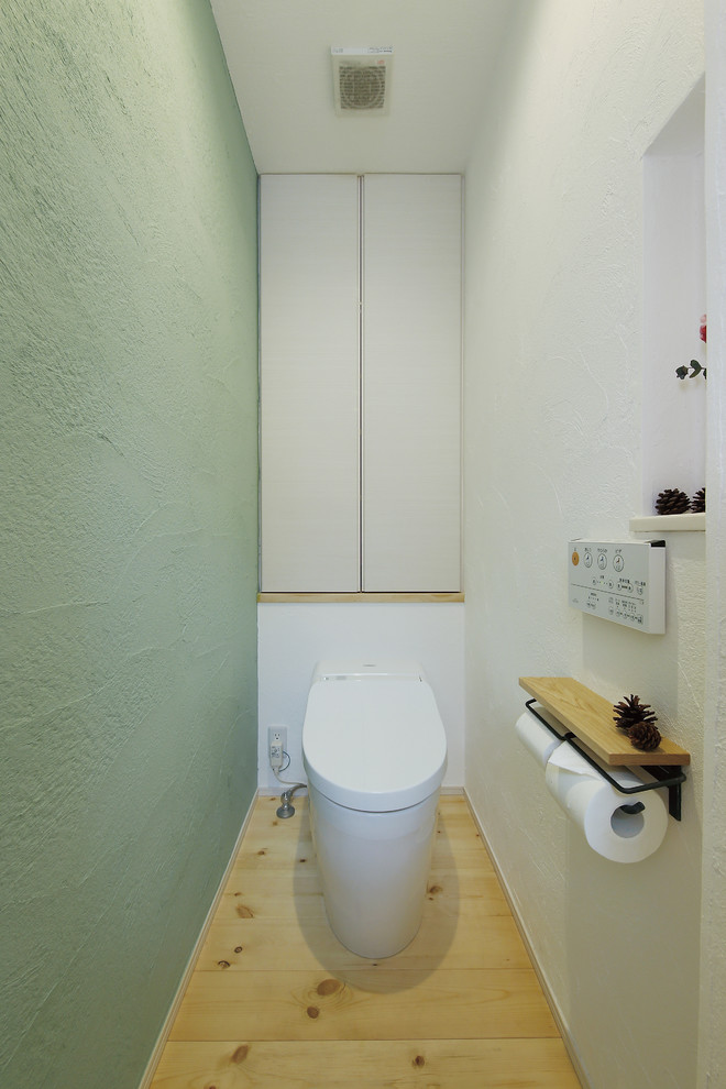 Nordische Gästetoilette mit Toilette mit Aufsatzspülkasten, grüner Wandfarbe und hellem Holzboden in Tokio