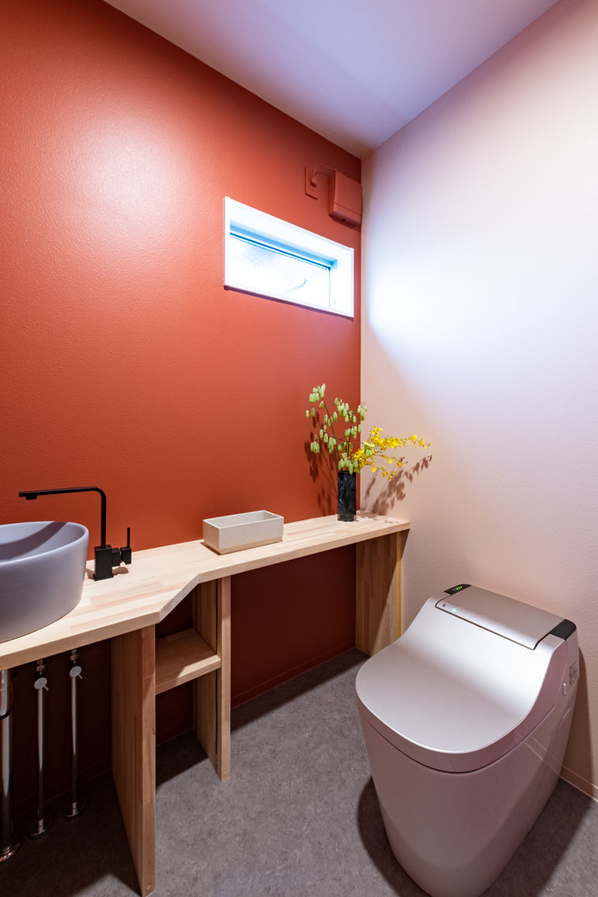 Пример оригинального дизайна: туалет в восточном стиле с оранжевыми стенами, настольной раковиной, столешницей из дерева, серым полом и коричневой столешницей