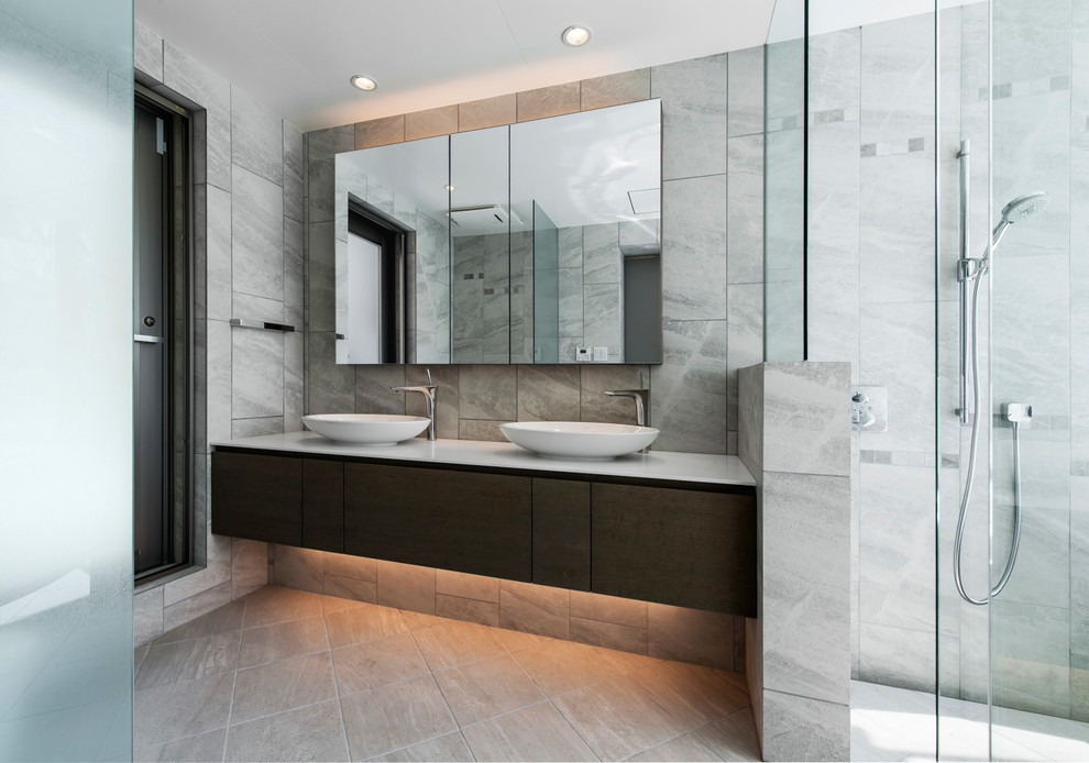 コンテンポラリースタイルのおしゃれな浴室 (濃色木目調キャビネット、グレーのタイル、グレーの壁、オーバーカウンターシンク、グレーの床、フラットパネル扉のキャビネット) の写真