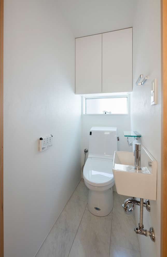 東京都下にあるシャビーシック調のおしゃれなトイレ・洗面所 (フラットパネル扉のキャビネット、一体型トイレ	、白い壁、ラミネートの床、壁付け型シンク、白い床) の写真