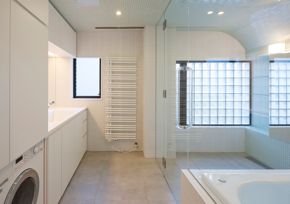 他の地域にある高級な広いモダンスタイルのおしゃれな浴室 (セラミックタイルの床、人工大理石カウンター、グレーの床、白い洗面カウンター、フラットパネル扉のキャビネット、白いキャビネット、一体型シンク) の写真