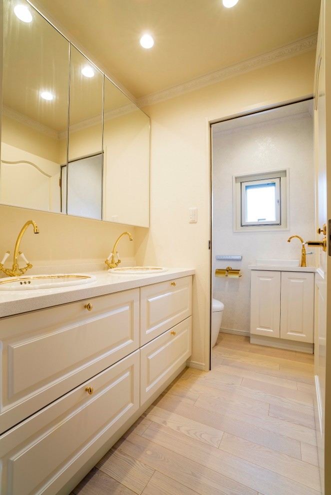 Inredning av ett klassiskt toalett, med luckor med upphöjd panel, vita skåp, vita väggar, målat trägolv, ett nedsänkt handfat och beiget golv