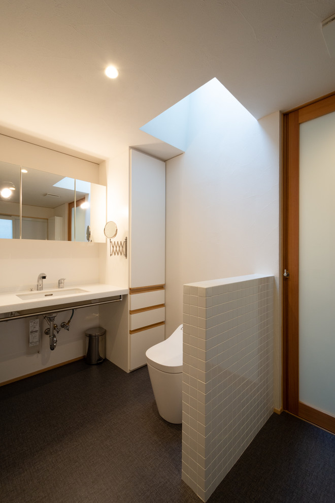 Aménagement d'un WC et toilettes moderne avec des portes de placard blanches, WC à poser, un carrelage blanc, des carreaux de céramique, un mur blanc, un sol en vinyl, un lavabo encastré, un plan de toilette en surface solide, un sol gris et un plan de toilette blanc.