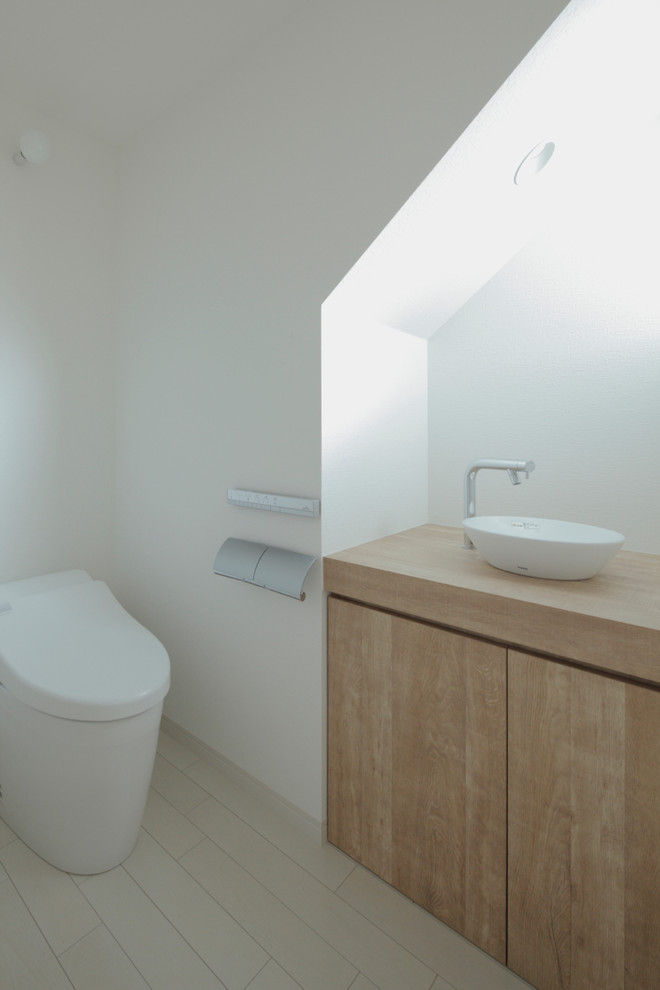 Design ideas for a modern cloakroom in Other with flat-panel cabinets, light wood cabinets, a one-piece toilet, white walls, a vessel sink, beige floors and beige worktops.