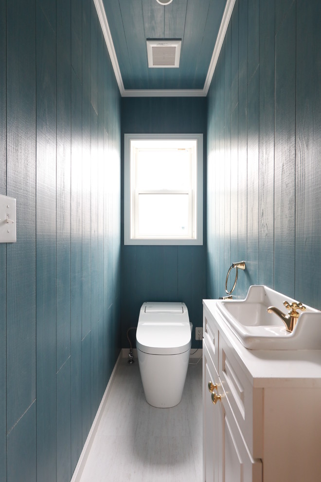 Bild på ett maritimt vit vitt toalett, med luckor med infälld panel, vita skåp, blå väggar, ett fristående handfat och vitt golv