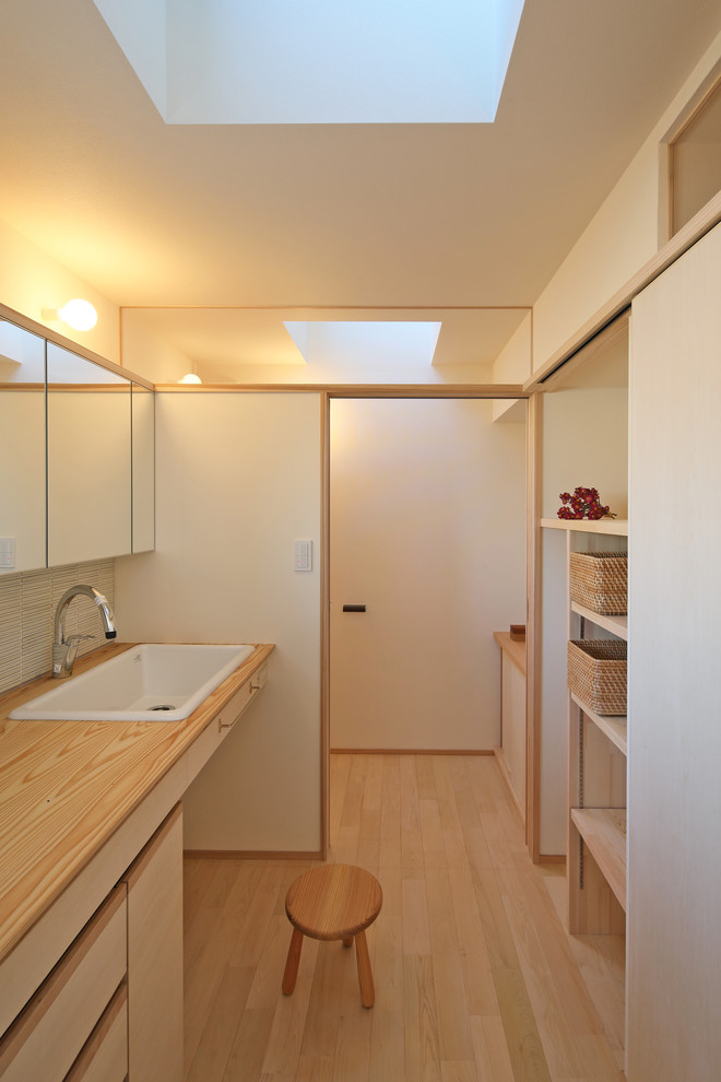 Cette image montre un WC et toilettes minimaliste avec un mur blanc, parquet clair, un lavabo posé, un placard à porte plane, des portes de placard beiges, un plan de toilette en bois, un sol beige et un plan de toilette marron.