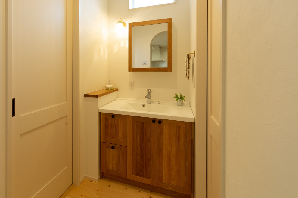 Modelo de aseo de pie de estilo de casa de campo con puertas de armario con efecto envejecido, paredes blancas, lavabo suspendido, encimeras marrones, papel pintado y papel pintado
