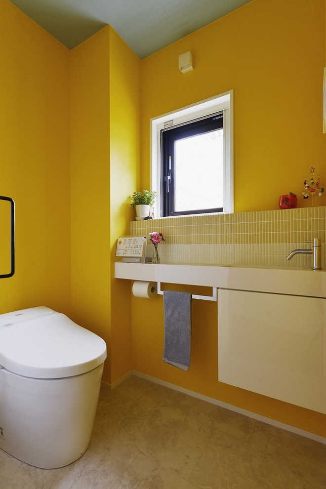 Bild på ett funkis toalett, med vita skåp, en toalettstol med hel cisternkåpa, gul kakel, gula väggar och ett integrerad handfat