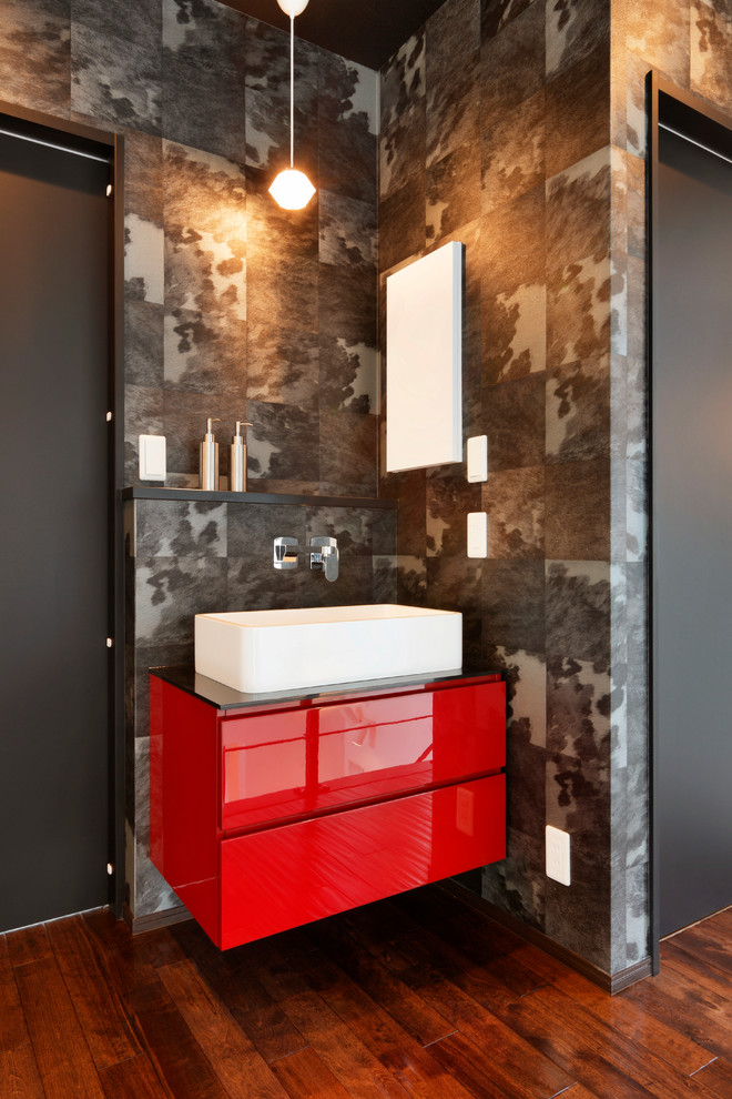 Cette photo montre un WC et toilettes moderne avec des portes de placard rouges, un carrelage gris, un mur gris, parquet foncé et un sol marron.