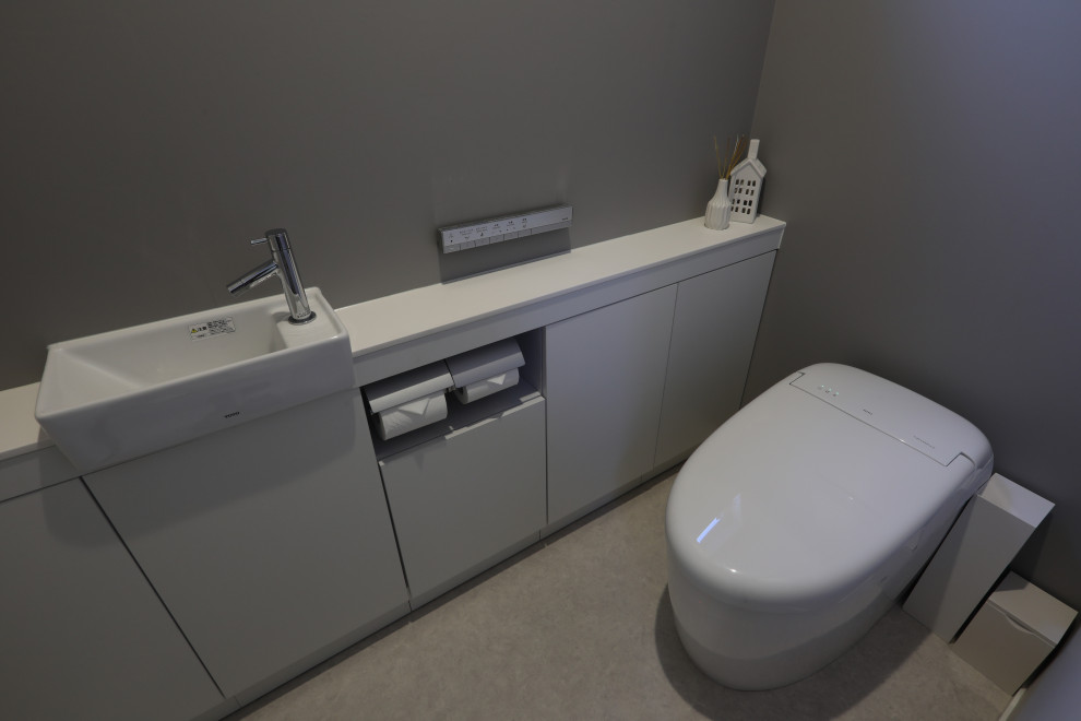 Idée de décoration pour un WC et toilettes minimaliste de taille moyenne avec des portes de placard blanches, WC à poser, un mur gris, un sol en vinyl, un sol beige et un plan de toilette blanc.
