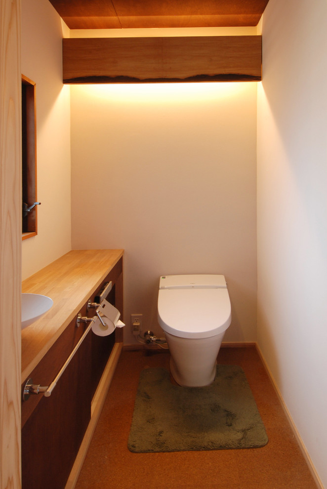 東京都下にあるアジアンスタイルのおしゃれなトイレ・洗面所 (フラットパネル扉のキャビネット、白い壁、ベッセル式洗面器、茶色い床) の写真