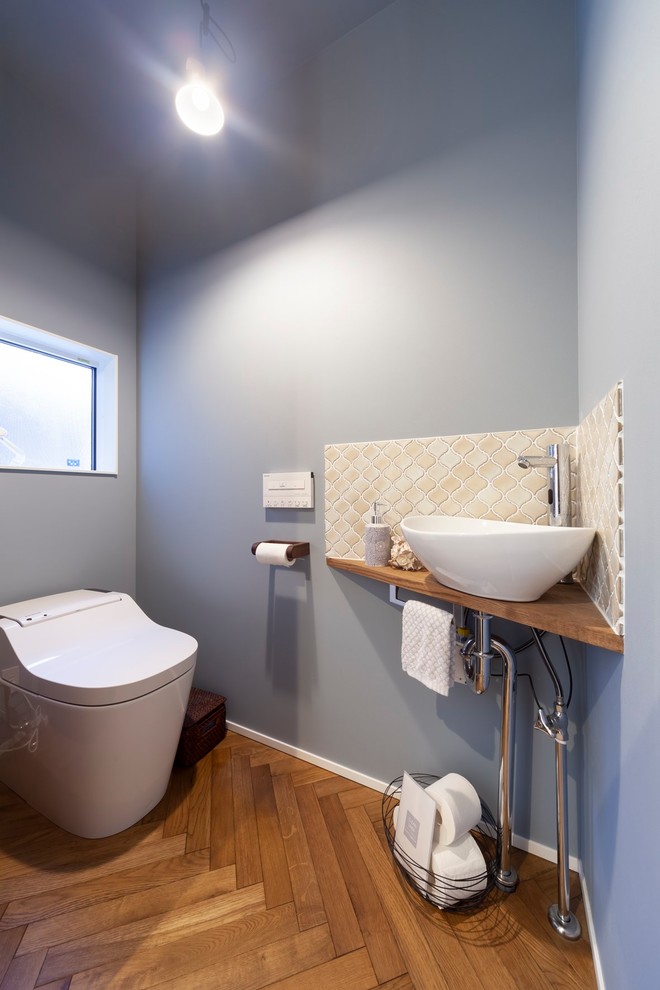 他の地域にある北欧スタイルのおしゃれなトイレ・洗面所 (ベージュのタイル、グレーの壁、茶色い床、ベッセル式洗面器、木製洗面台) の写真