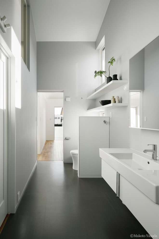 Inspiration pour un WC et toilettes minimaliste de taille moyenne avec un placard à porte plane, des portes de placard blanches, WC à poser, un carrelage gris, un mur blanc, un sol en linoléum, un lavabo intégré, un sol gris et un plan de toilette blanc.