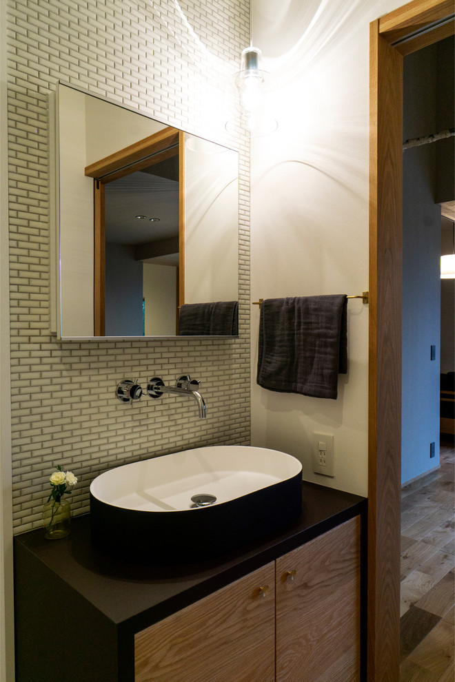 На фото: туалет в стиле модернизм с белыми стенами, паркетным полом среднего тона, настольной раковиной и коричневым полом