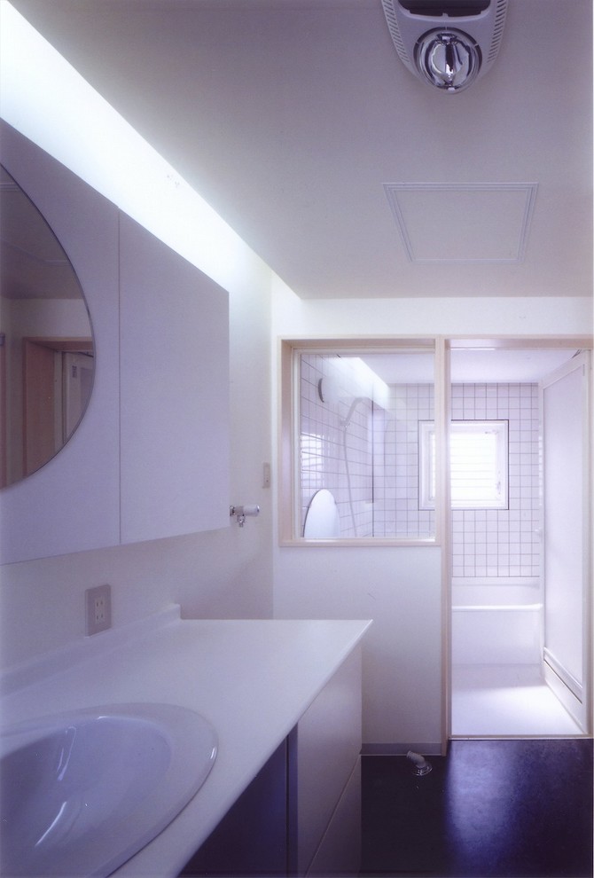 Inspiration pour un WC et toilettes minimaliste avec un placard à porte plane, des portes de placard blanches, un mur blanc, un sol en liège, un lavabo posé, un plan de toilette en surface solide et un sol noir.