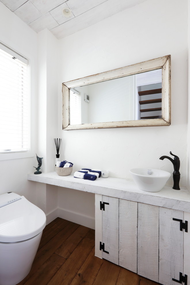 Cette image montre un WC et toilettes marin avec un mur blanc, parquet foncé, une vasque et un sol marron.