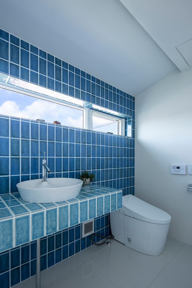Идея дизайна: туалет среднего размера в стиле модернизм с унитазом-моноблоком, синей плиткой, керамогранитной плиткой, синими стенами, полом из керамогранита, настольной раковиной, столешницей из плитки, белым полом и бирюзовой столешницей