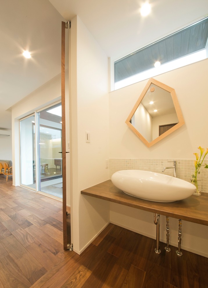 Foto di un bagno di servizio etnico con piastrelle beige, pareti bianche, lavabo a bacinella, top in legno, pavimento in legno massello medio, pavimento marrone e top marrone