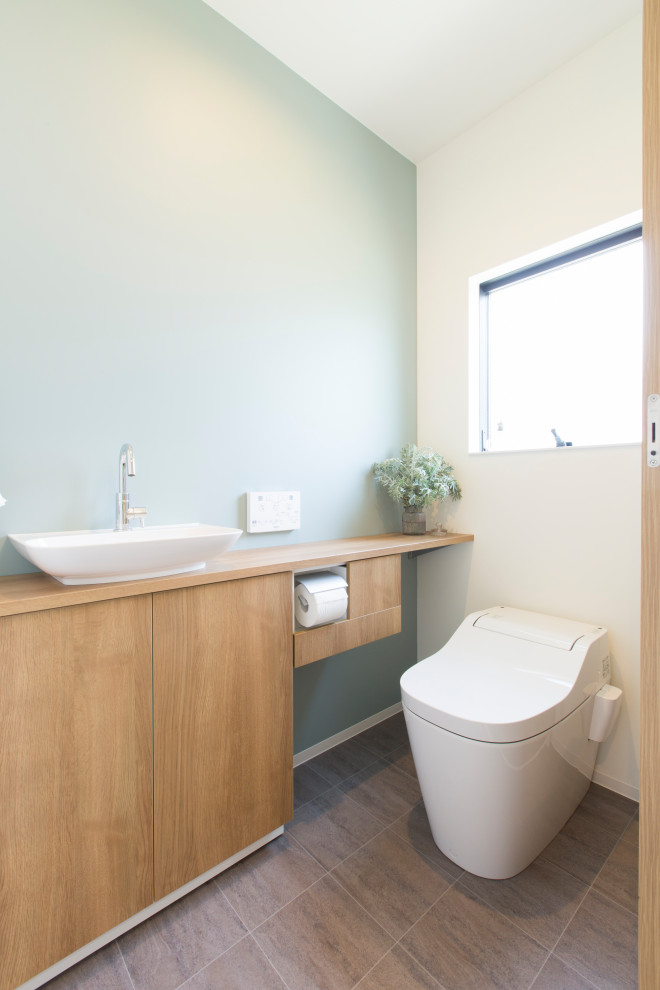 Bild på ett nordiskt brun brunt toalett, med öppna hyllor, skåp i mellenmörkt trä, en toalettstol med hel cisternkåpa, grå kakel, vita väggar, vinylgolv, ett nedsänkt handfat och grått golv