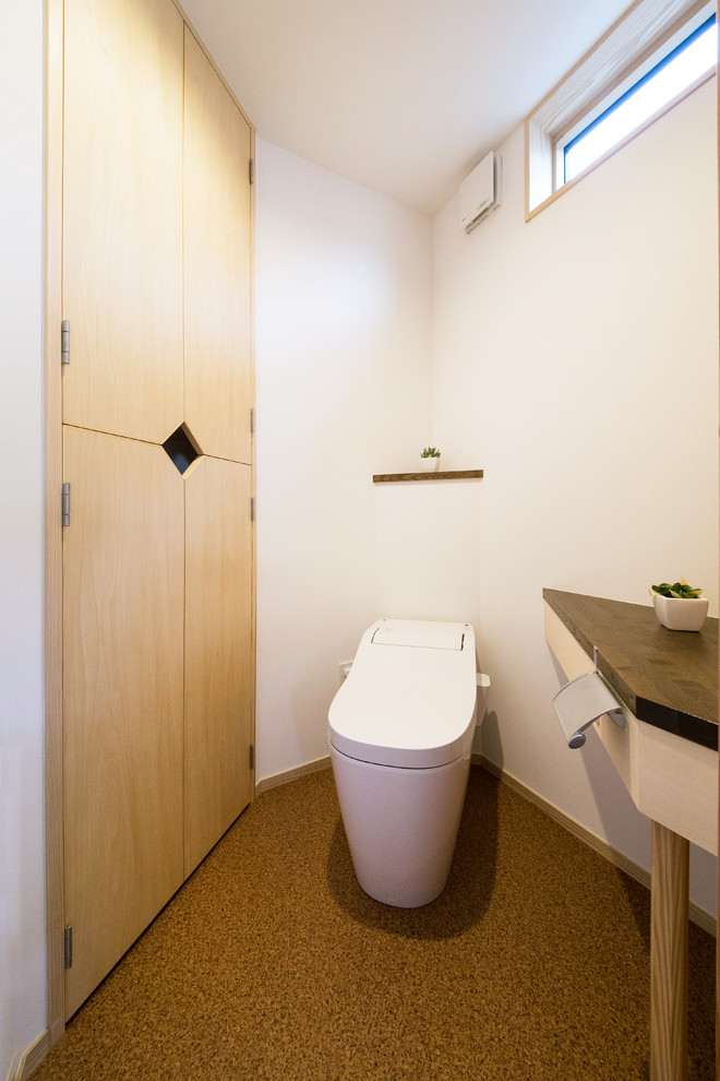 Idée de décoration pour un WC et toilettes asiatique avec un mur blanc et un sol marron.