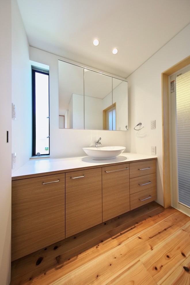 Exemple d'un WC et toilettes asiatique en bois brun avec un placard à porte plane, un mur blanc, un sol en bois brun, une vasque, un sol marron et un plan de toilette blanc.