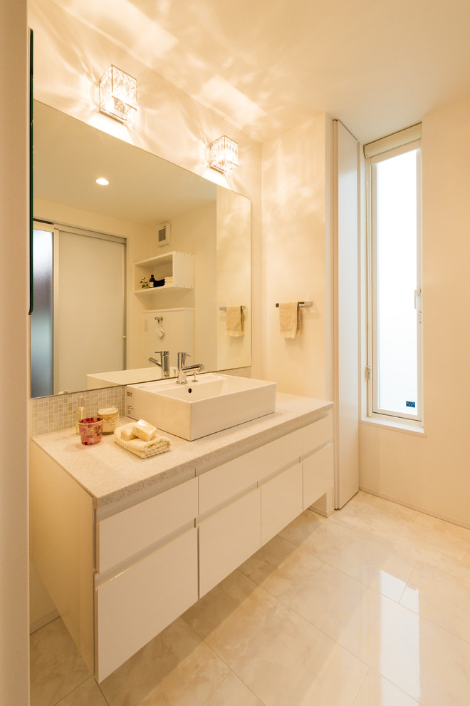 Aménagement d'un WC et toilettes asiatique avec un placard à porte plane, des portes de placard blanches, un mur blanc, un sol en marbre, une vasque, un sol beige et un plan de toilette blanc.