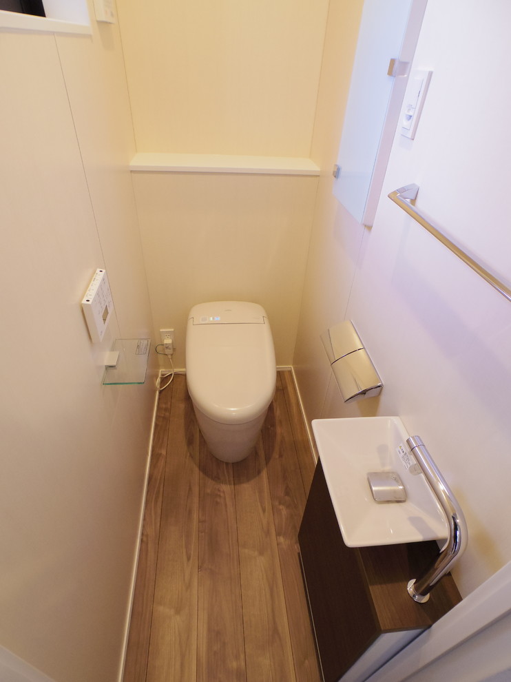 Idee per un bagno di servizio nordico con ante lisce, ante in legno bruno, WC monopezzo, pareti beige, pavimento in compensato, lavabo a bacinella e pavimento marrone