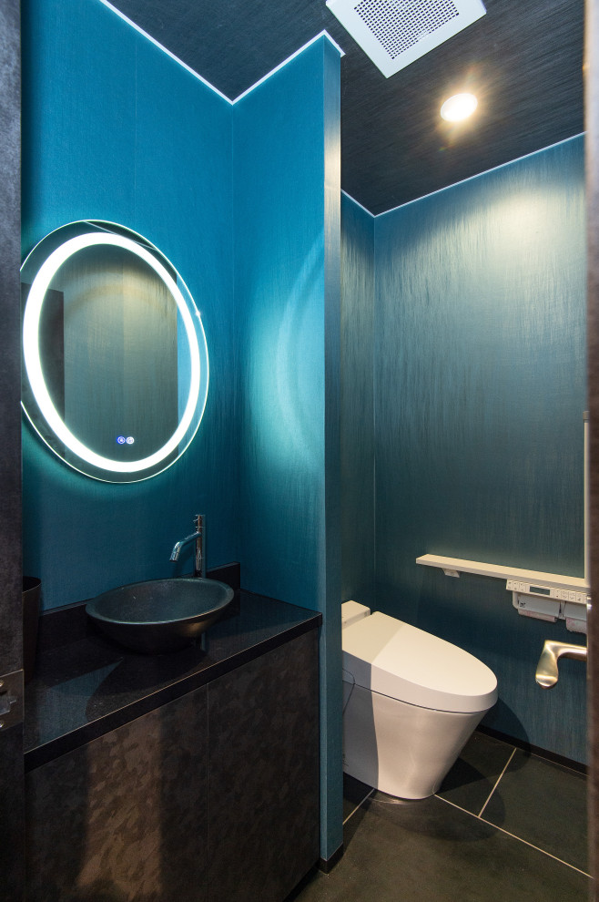 Inredning av ett modernt stort svart svart toalett, med släta luckor, svarta skåp, en toalettstol med hel cisternkåpa, blå väggar, plywoodgolv, ett fristående handfat, bänkskiva i akrylsten och svart golv