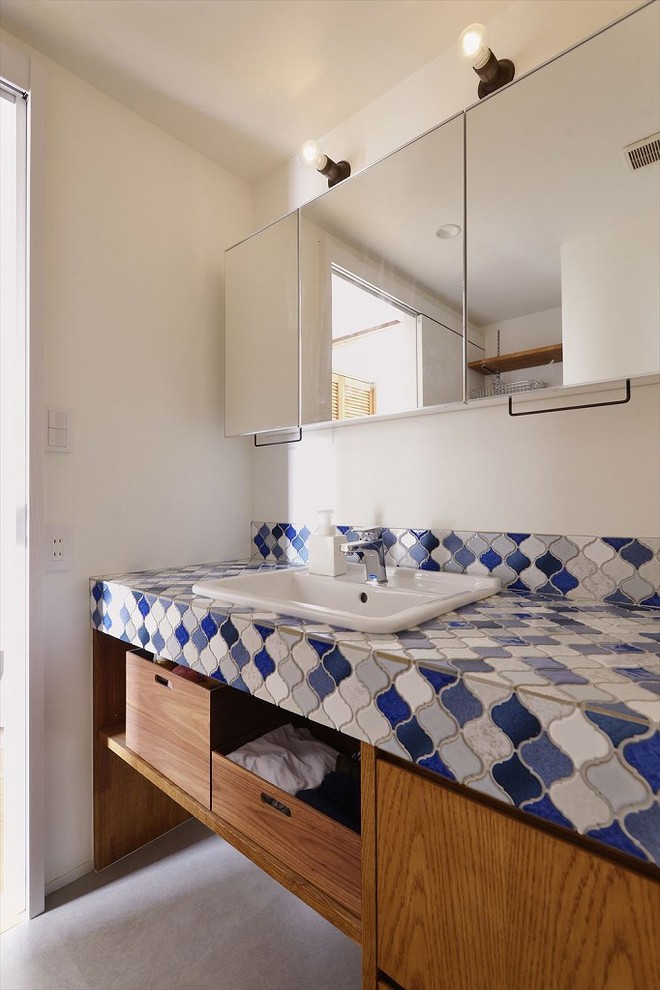 Réalisation d'un WC et toilettes méditerranéen en bois brun avec un mur blanc, sol en béton ciré, un lavabo posé, un plan de toilette en carrelage, un sol gris et un plan de toilette bleu.