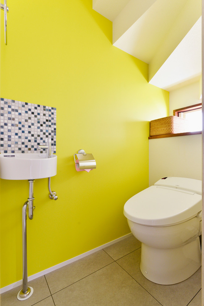 Idée de décoration pour un WC et toilettes design avec un mur jaune, un plan vasque et un sol gris.
