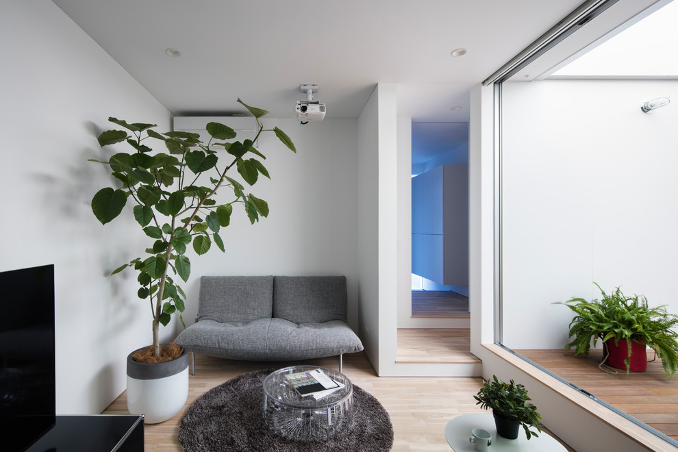 На фото: маленькая гостиная комната в стиле модернизм с белыми стенами, светлым паркетным полом, отдельно стоящим телевизором и коричневым полом для на участке и в саду с