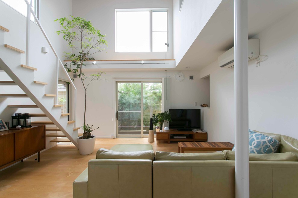 Offenes Modernes Wohnzimmer mit weißer Wandfarbe, hellem Holzboden, freistehendem TV und braunem Boden in Sonstige