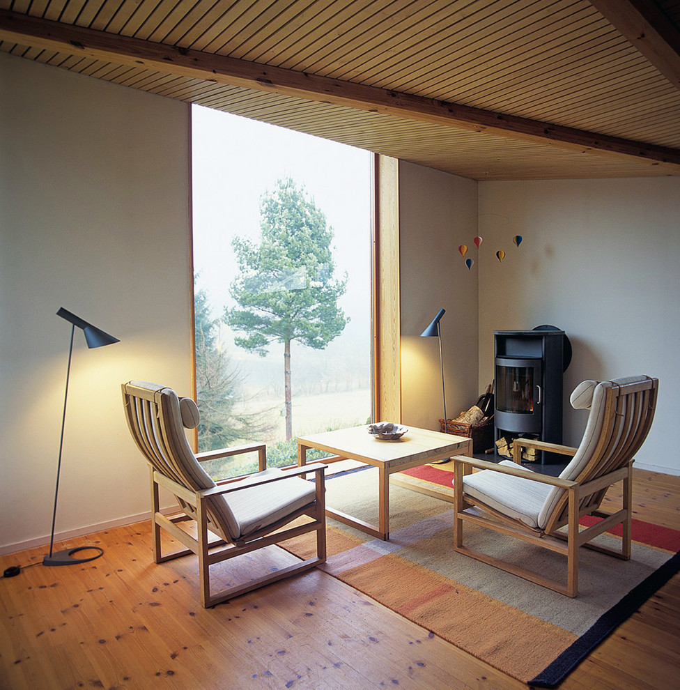 Modelo de sala de estar de estilo zen con paredes blancas, suelo de madera en tonos medios y estufa de leña