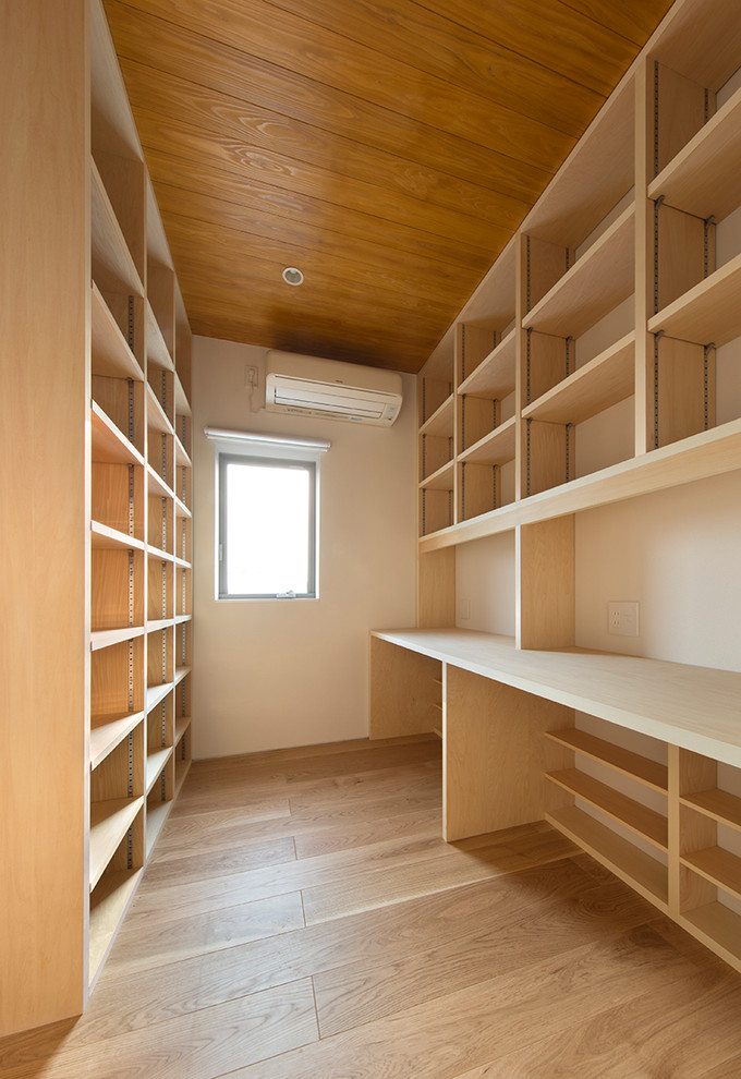 Imagen de sala de estar con biblioteca cerrada moderna pequeña sin televisor con paredes blancas, suelo de contrachapado y suelo beige