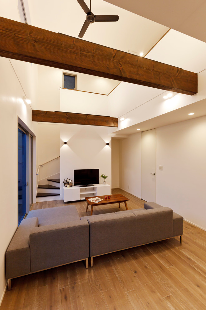Modelo de sala de estar abierta contemporánea sin chimenea con paredes blancas, suelo de madera clara, televisor independiente y suelo beige