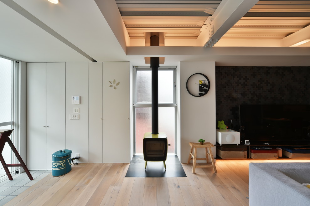 Urban games room in Nagoya with white walls, light hardwood flooring, a wood burning stove and brown floors.