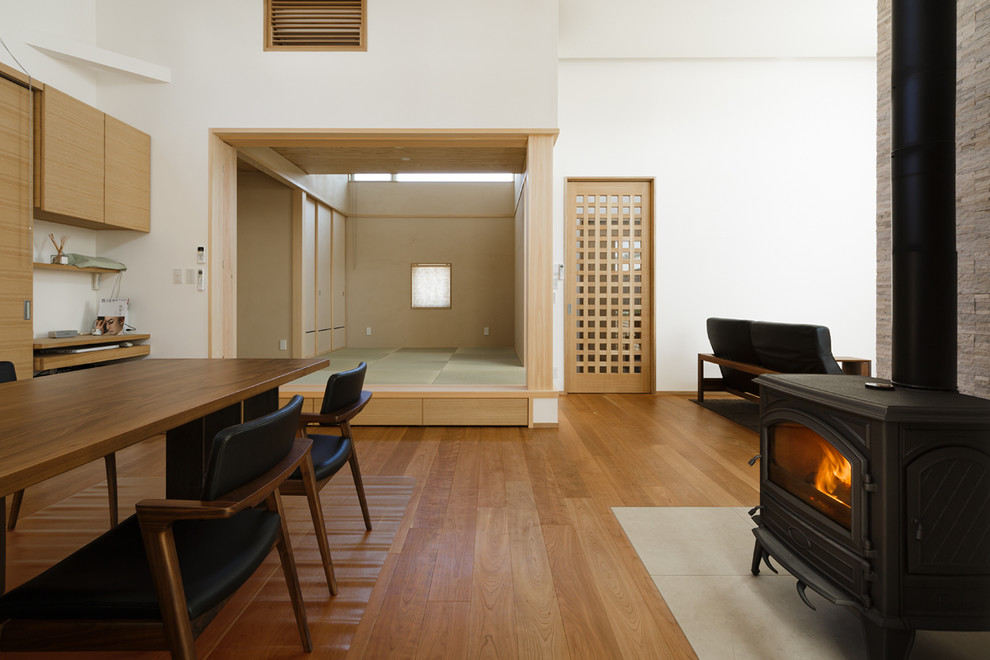 Foto de sala de estar asiática con paredes blancas, suelo de madera en tonos medios, estufa de leña, marco de chimenea de piedra y suelo marrón