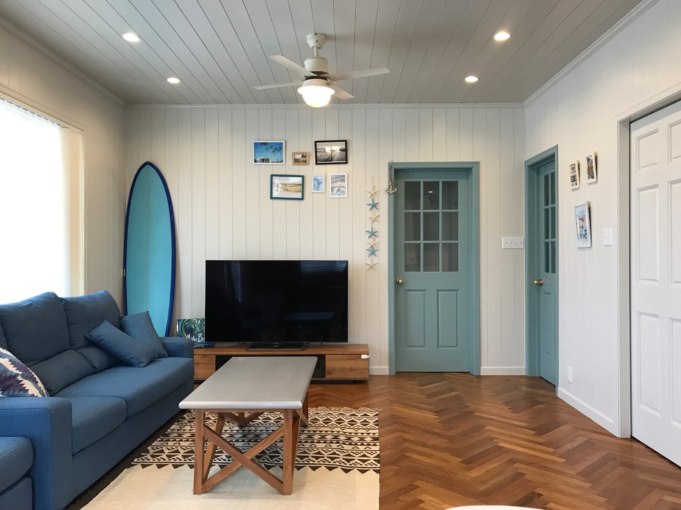 他の地域にあるビーチスタイルのおしゃれな独立型ファミリールーム (白い壁、濃色無垢フローリング、据え置き型テレビ、茶色い床、青いソファ) の写真